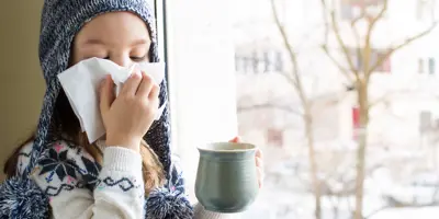 Una niña pequeña con ropa de invierno sonándose la nariz con un pañuelo de papel.
