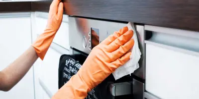 Una persona limpiando el exterior de un horno con un paño y guantes de color naranja