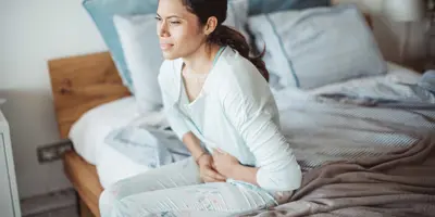 Una mujer sentada en su cama con dolor de estómago a causa de la diarrea.